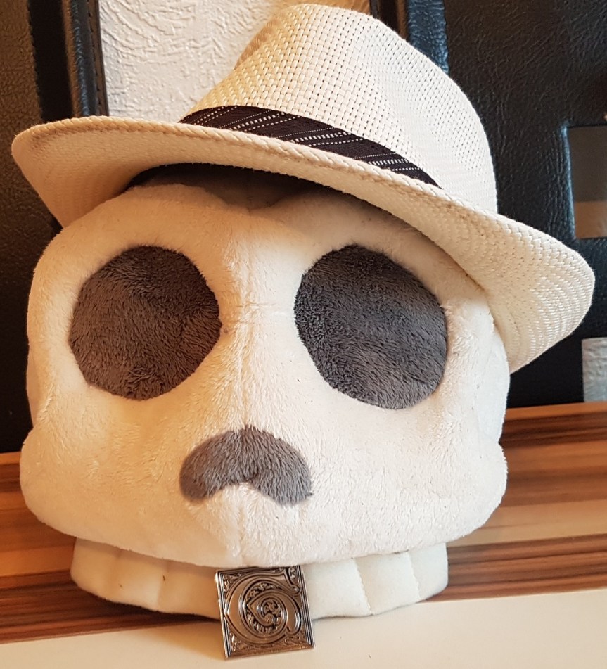 Giovanni Fan Schädel (Plüsch-Schädel mit Gangsterhut und einem Giovanni Pin an den Zähnen)